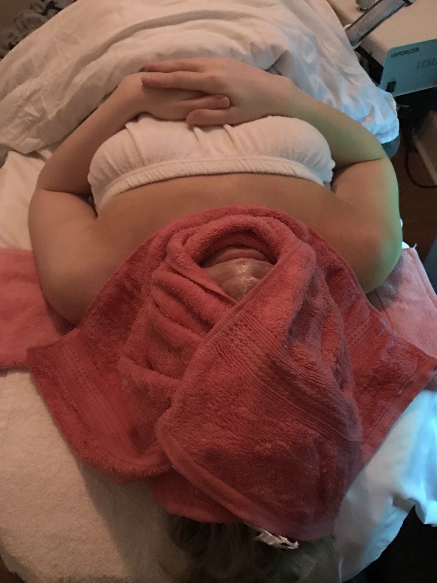 A woman with her head wrapped in a pink towel receiving a treatment